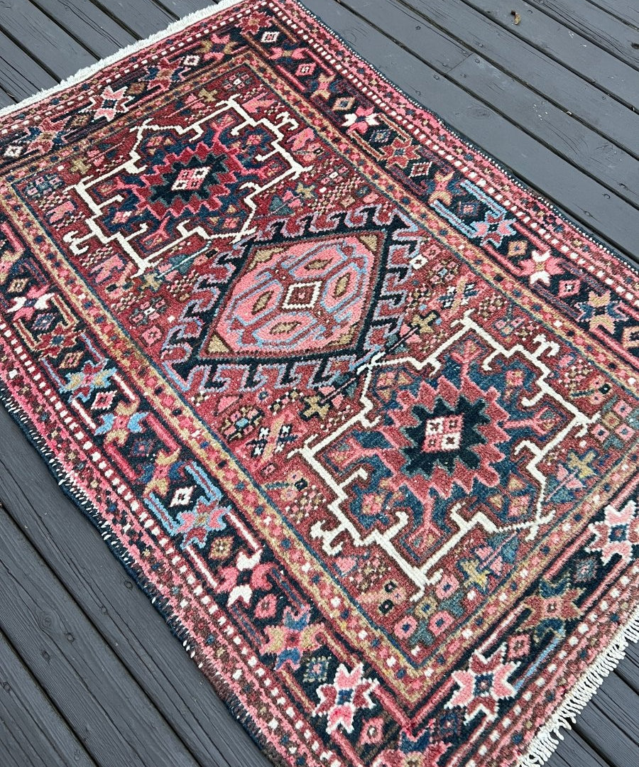 Persian Karaja rug angled close-up with maroon diamond motifs and white fringe.