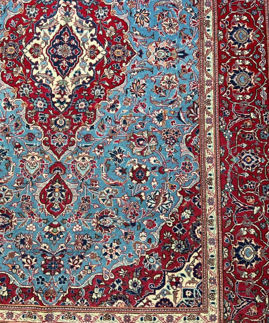 Persian-style rug with blue field, red border, ornate floral medallion pattern, fringed