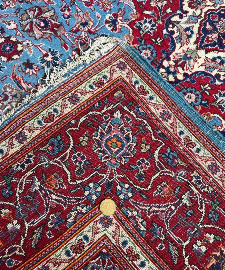 Rug close-up with red and blue floral and geometric pattern, bordered corner and trim