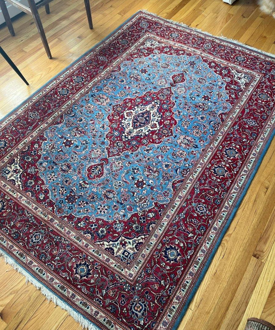 Blue rug with red border and central medallion, detailed floral motifs, light fringe visible