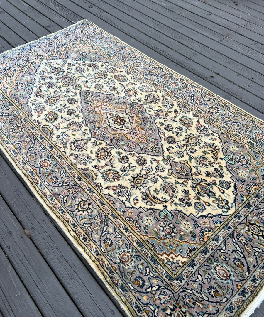 Persian Kashan rug corner view, cream background with ornate blue and gold motifs