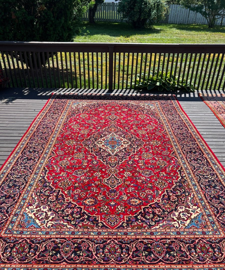 Persian Kashan rug on wooden deck with red medallion, navy corner motifs, cream border