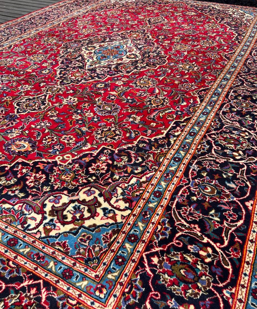 Persian Kashan rug with red patterned field, navy swirls, cream and blue trim on edges