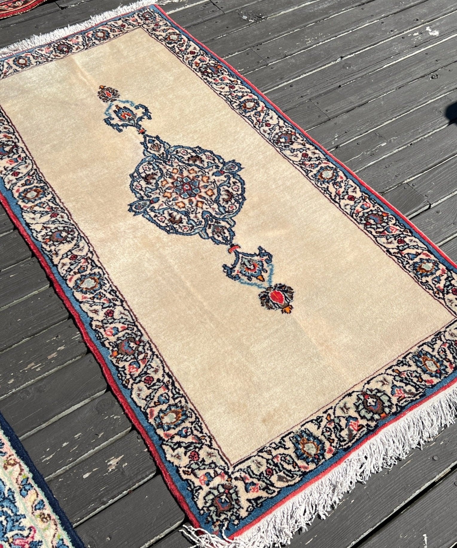 Cream Kashan rug with blue and red center medallion, navy border, white fringes