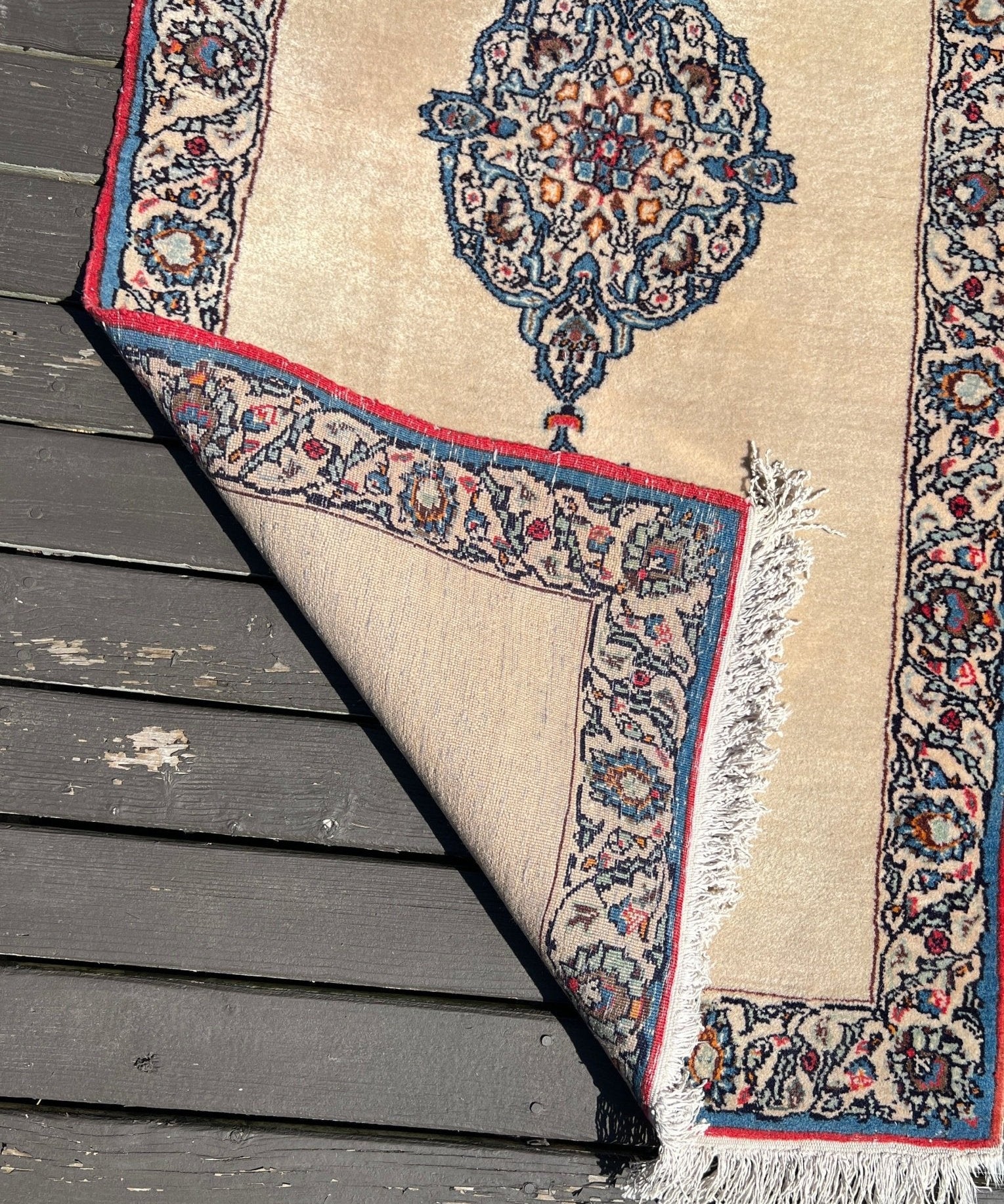 Triangular corner view of cream Kashan rug with navy border and fringe on edge