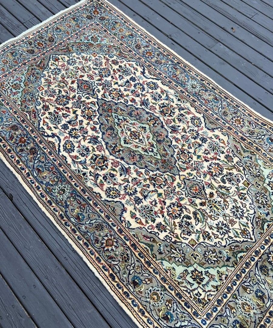 Persian Kashan rug, angled view with cream medallion center and navy blue border lines