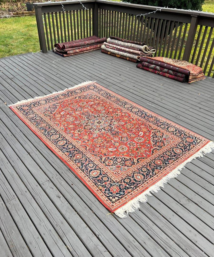 Kashan rug with red design and fringed edges on outdoor wooden deck