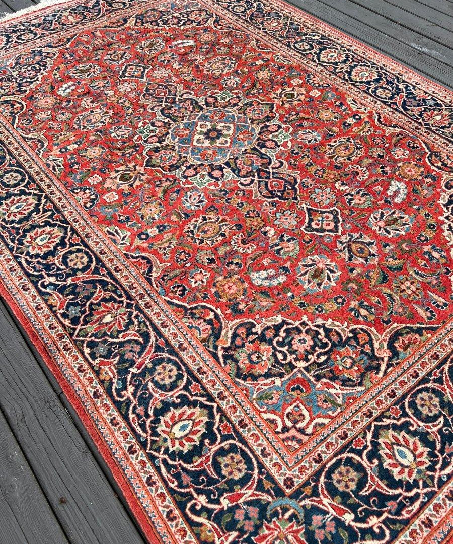 Kashan rug diagonal view with red field, navy border and floral motifs