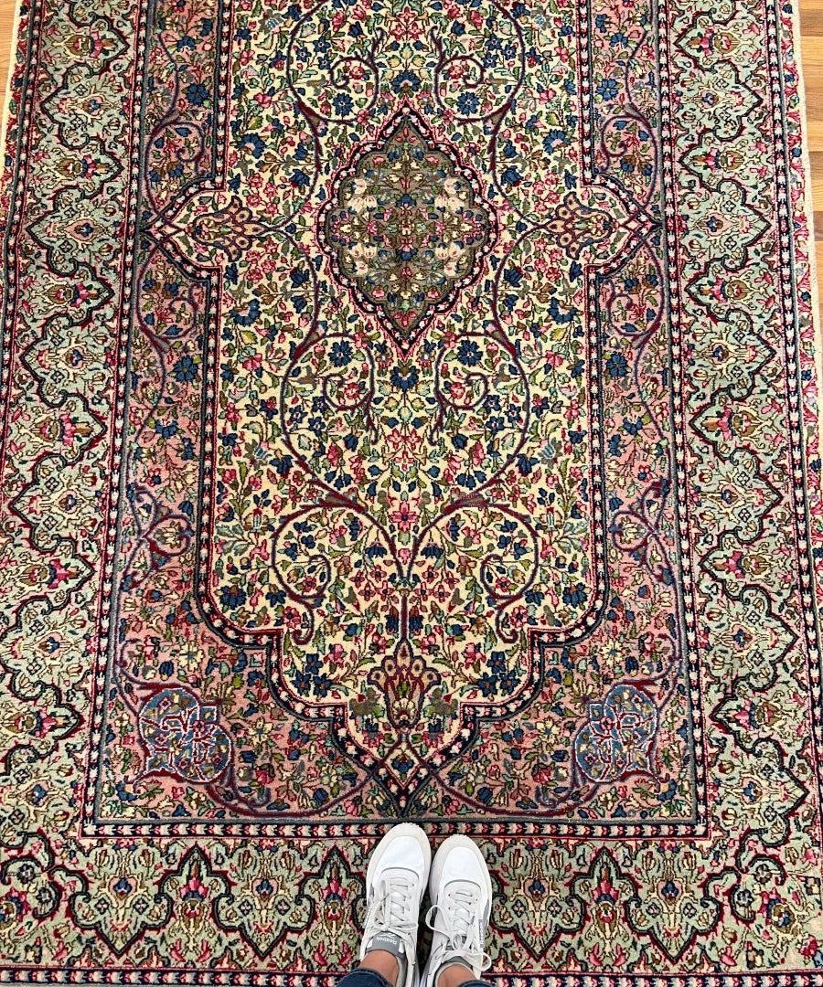 Persian rug full view with cream background, dense floral center, and red border