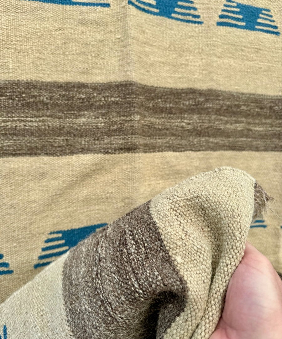 Persian kilim rug close-up corner: beige weave, blue motifs, dark stripe, short fringe