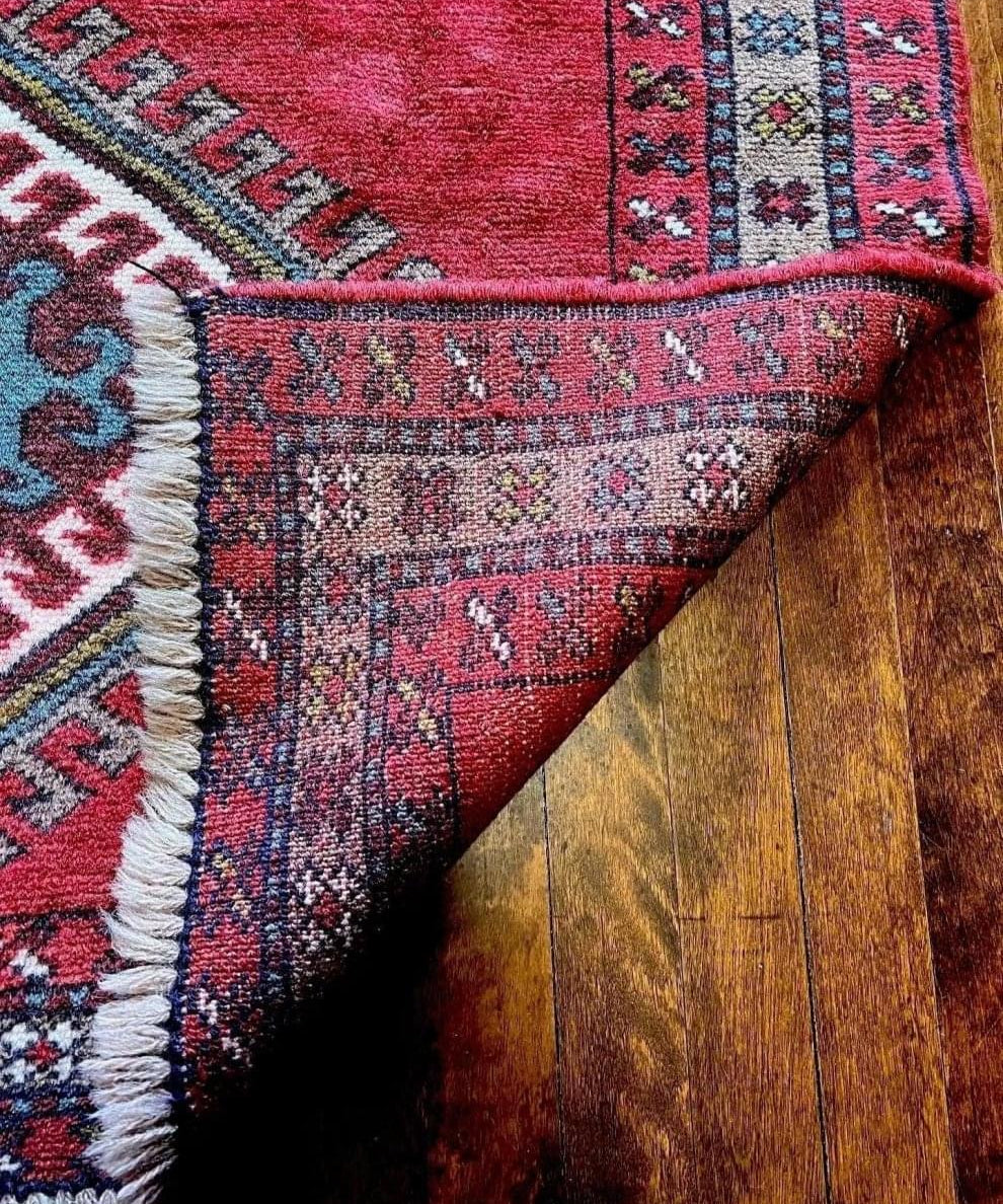 Corner detail of red rug with geometric border and cream fringe on wood floor