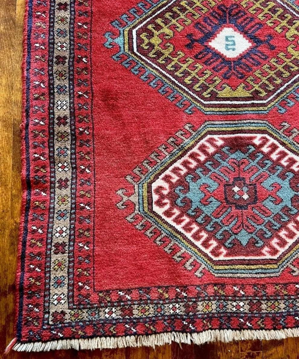 Red rug with blue, teal, and navy medallion patterns and cream fringe edge