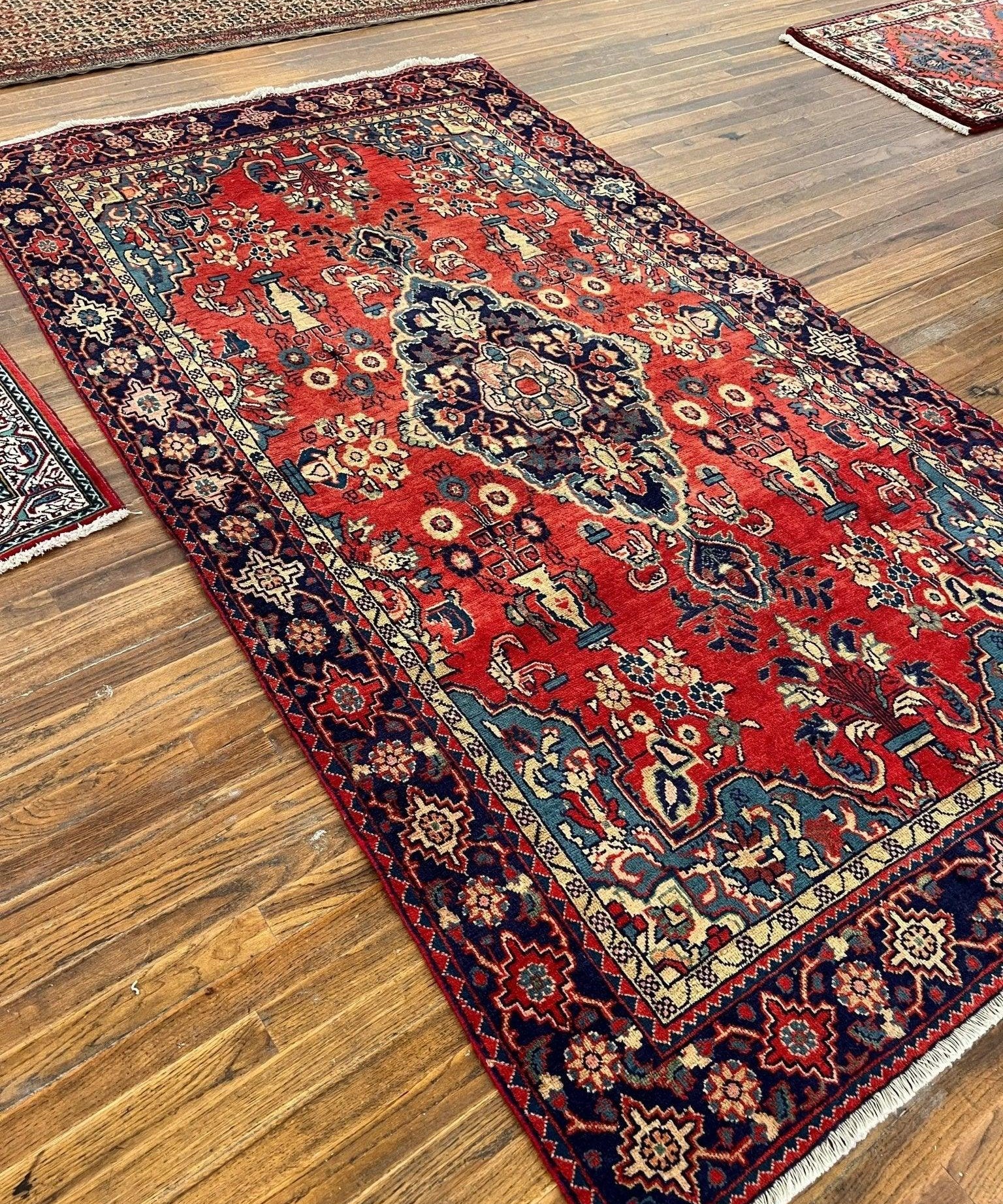 Red Persian-style rug diagonal view, detailed medallion and corner rosettes with navy border.
