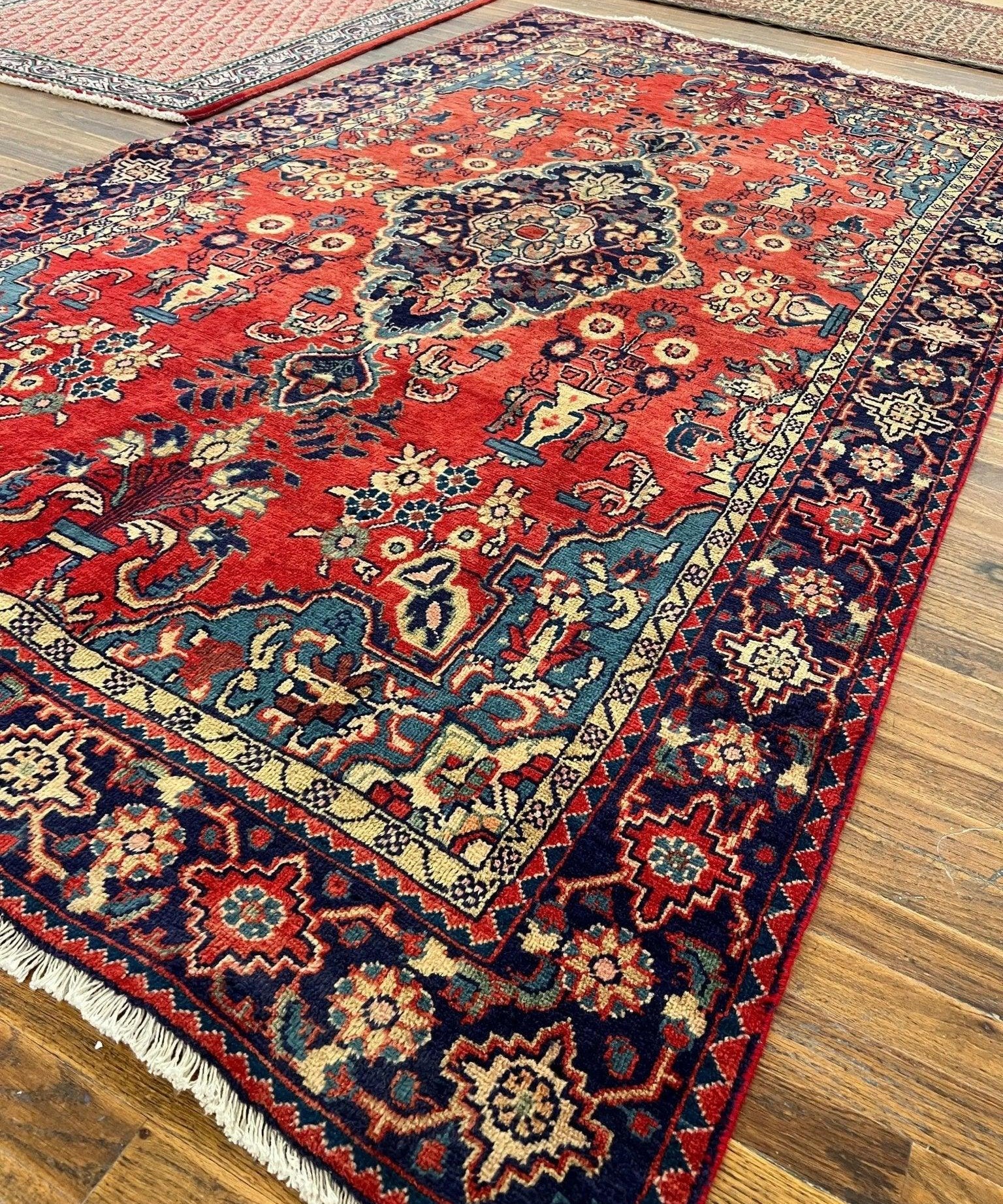 Red Persian-style rug close-up with central medallion, geometric motifs, navy edge fringe.