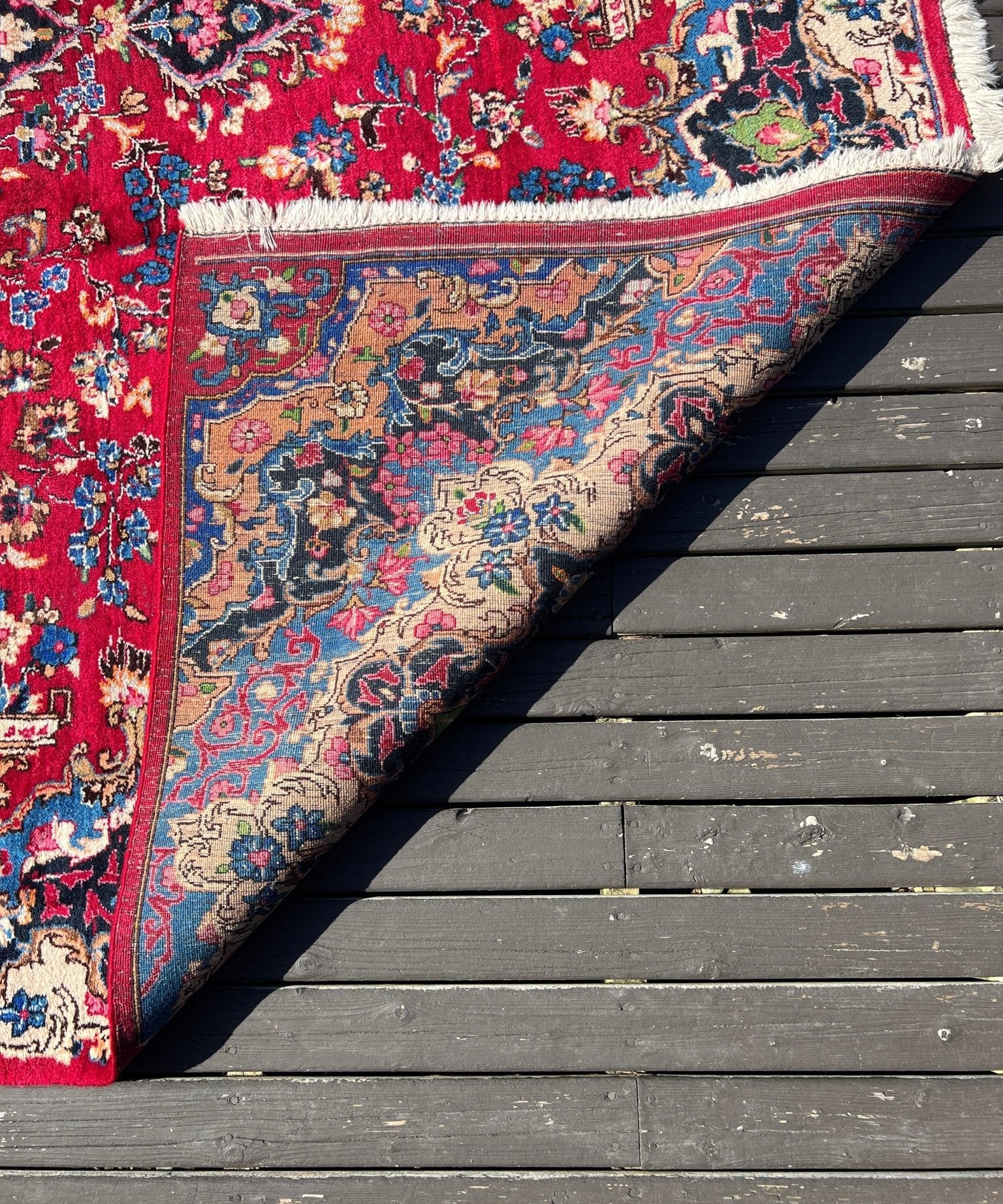 Red rug corner with ornate border, multicolor vines and floral motifs