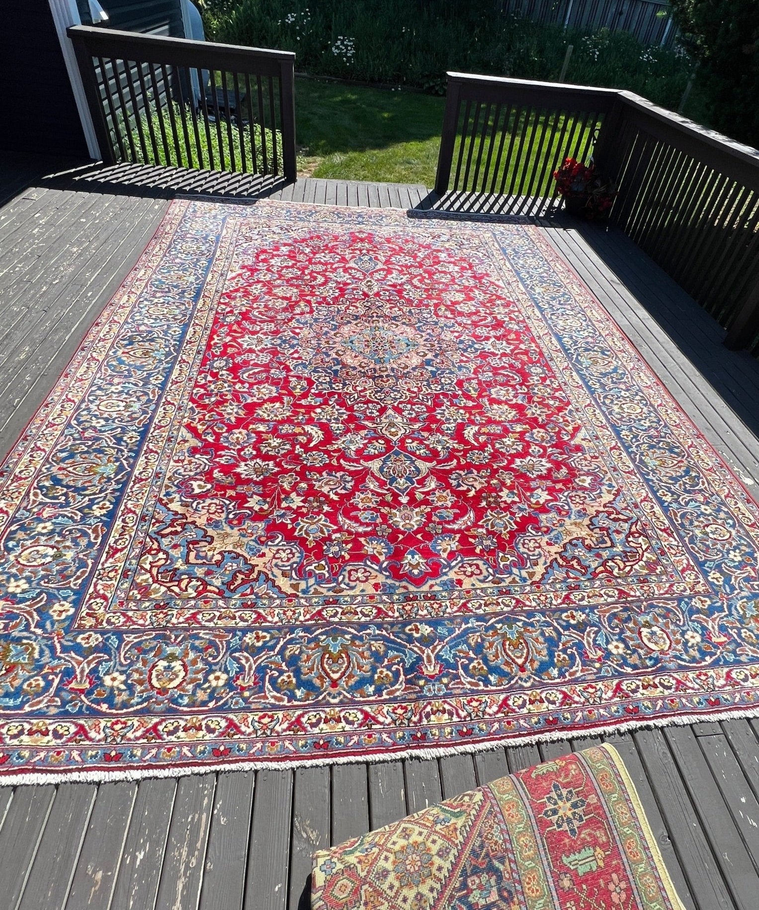 Persian-style rug with red center medallion and blue floral border on an outdoor deck