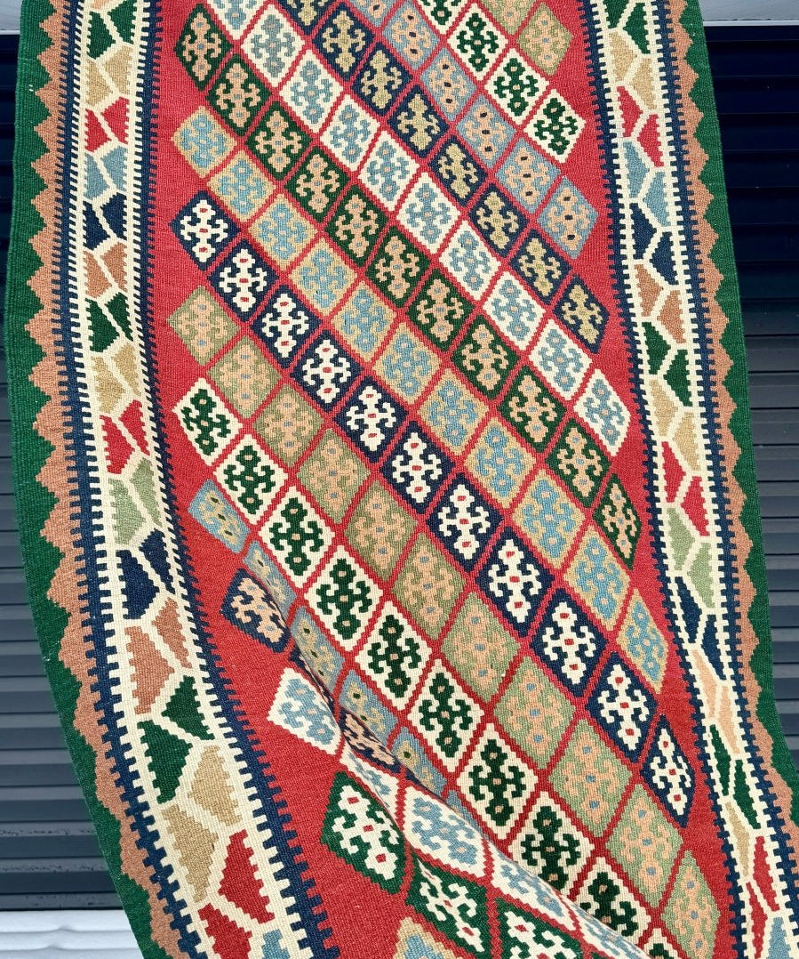 Kilim rug with red, blue, and green diamond pattern, trimmed with white fringe