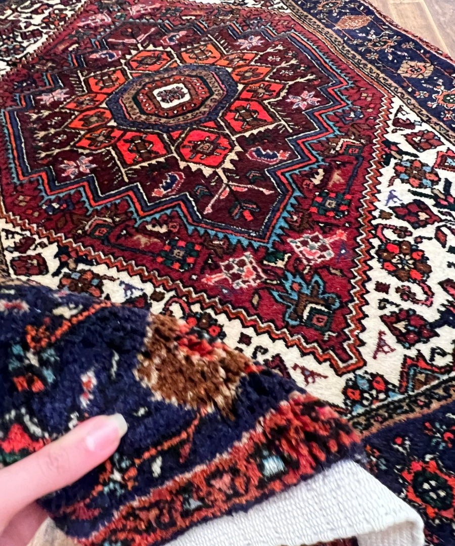 Rug corner close-up with red, navy, and white geometric pattern; hand lifts edge