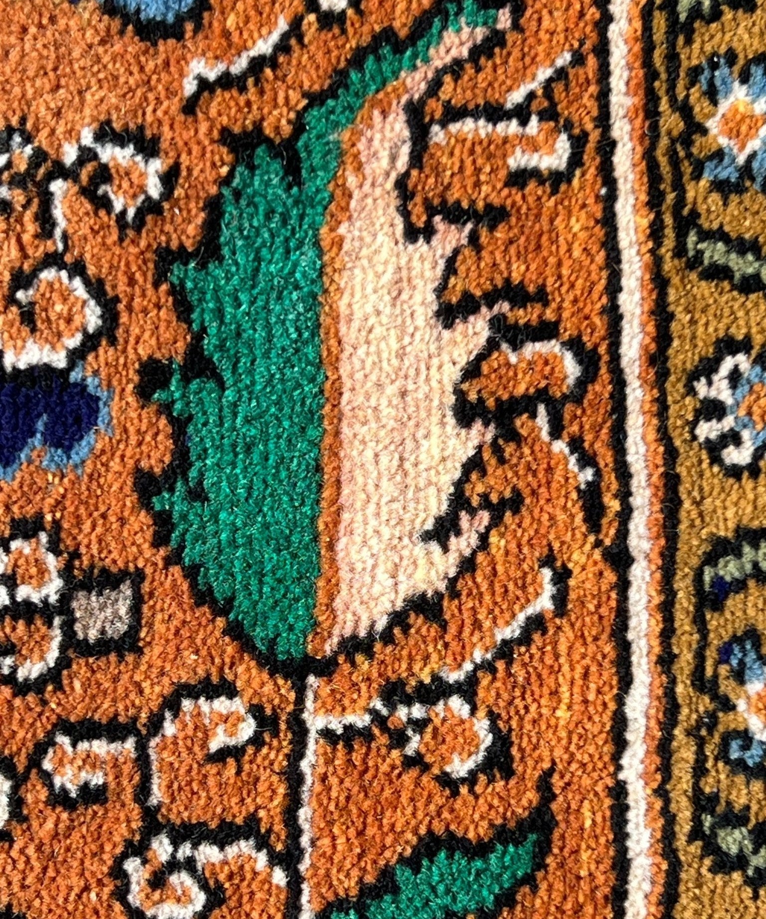 Close-up rug pile with teal leaf motif on orange and navy ornamental background