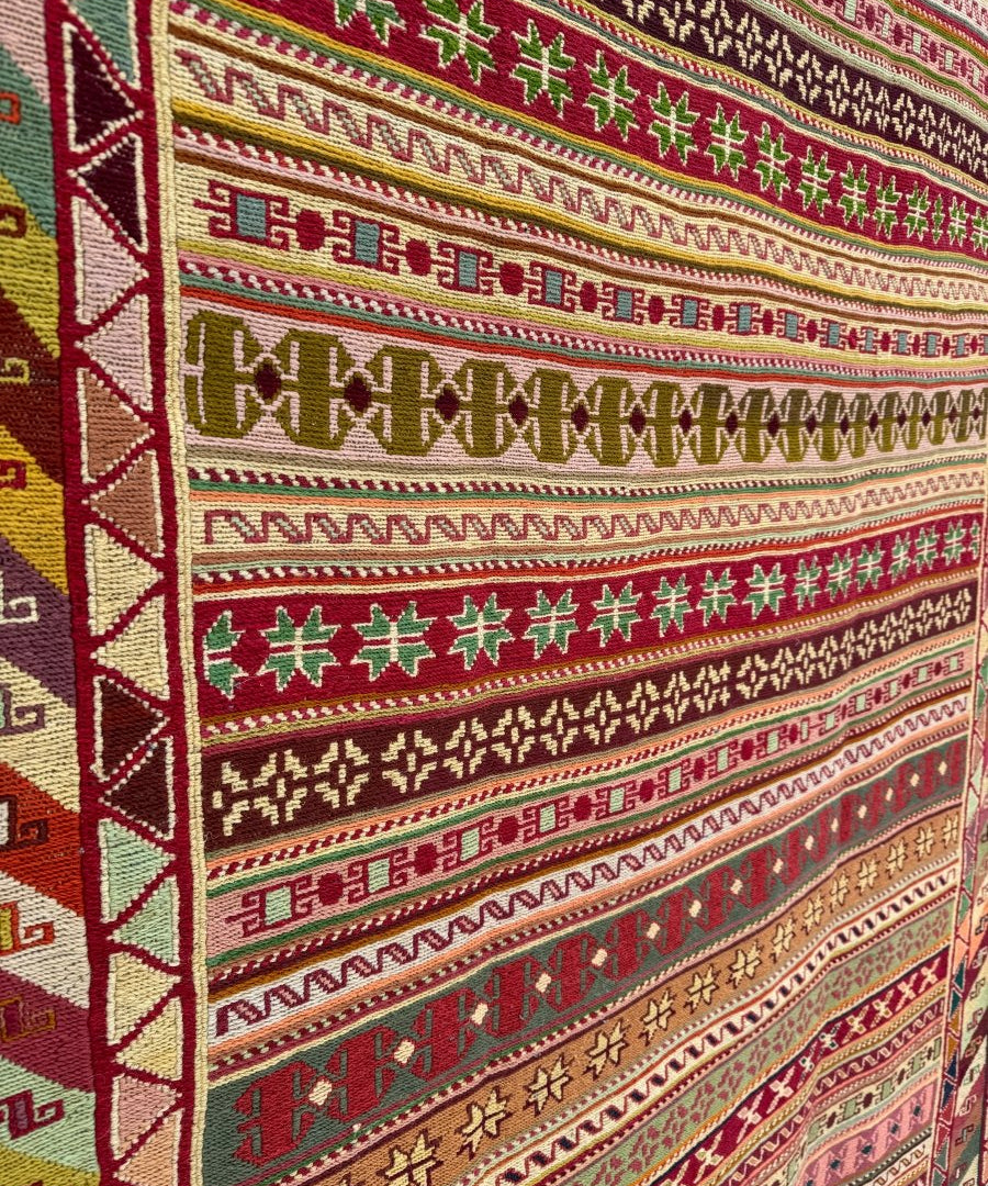Kilim rug close-up with geometric stripes in green, red, beige, and dark maroon