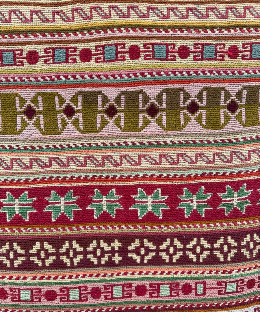 Striped kilim rug with repeating geometric motifs in red, green, cream, and dark accents