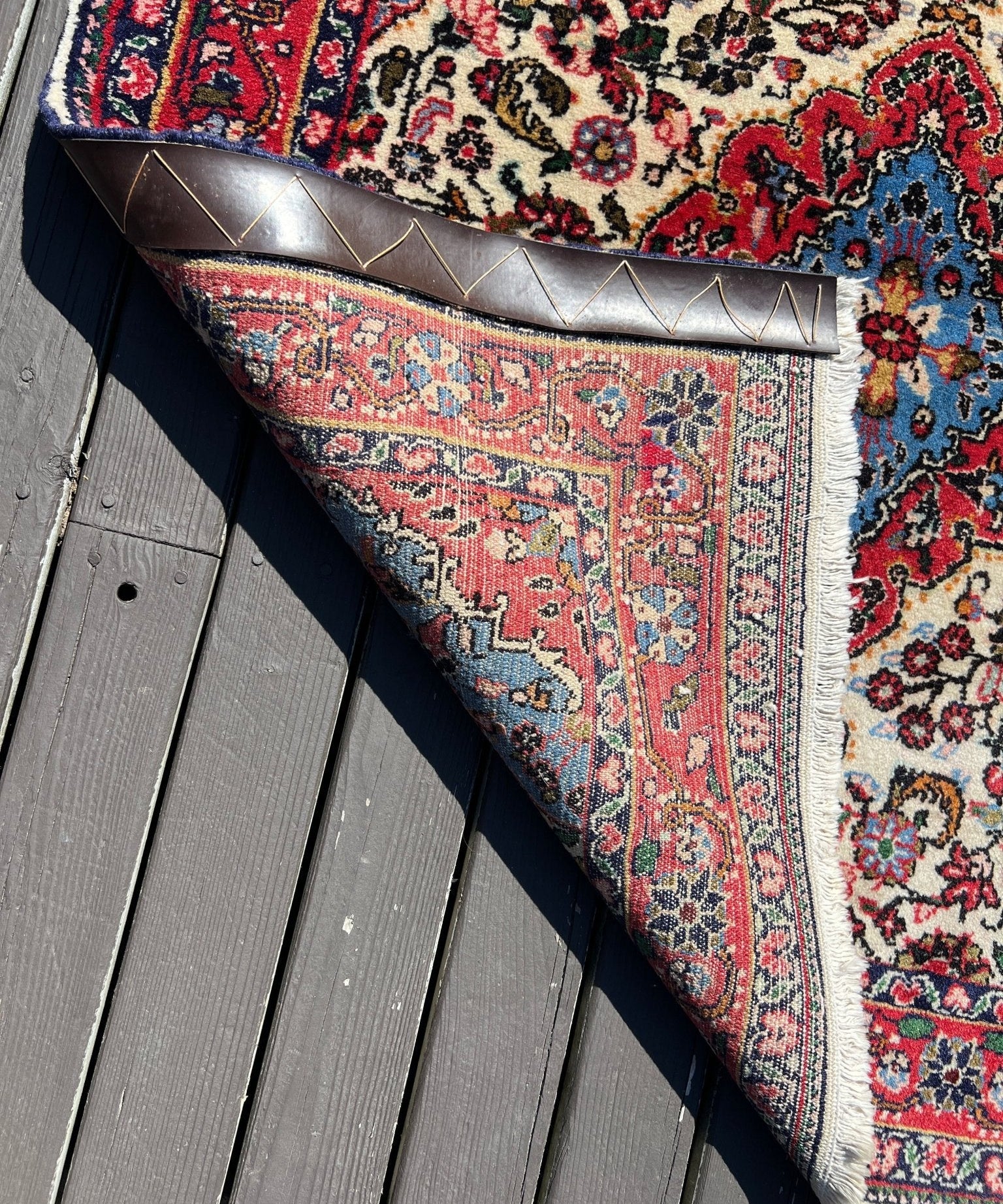 Persian rug corner with fringe, red border and blue floral motifs on cream
