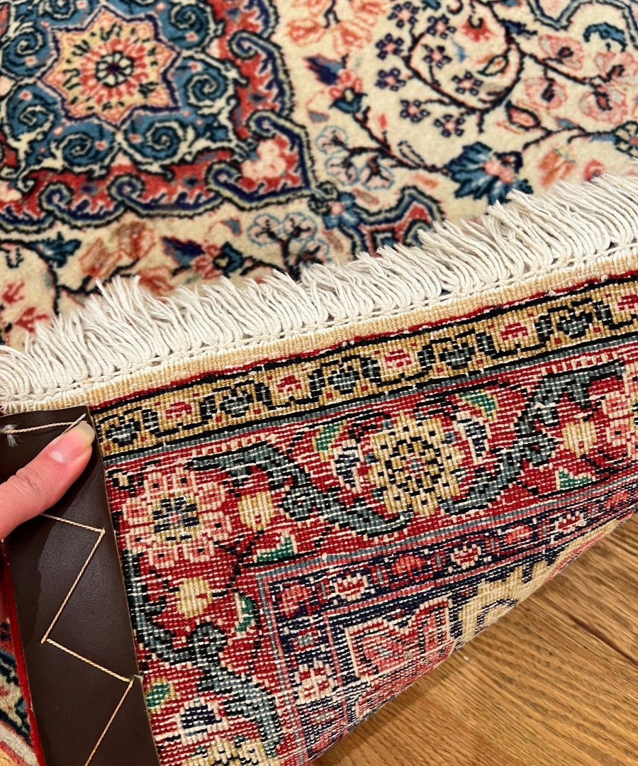 Sarouk rug corner detail, cream background with red blue geometric border and fringe edge