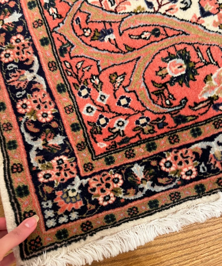 Persian Sarouk rug corner detail with red floral motifs, dark border, and cream background