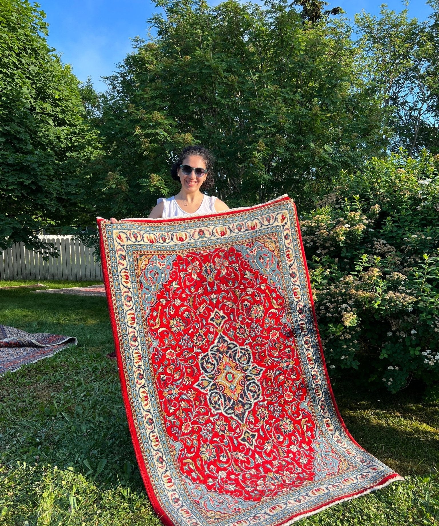 Persian Sarouk rug with red floral medallion and blue border, full view on grass