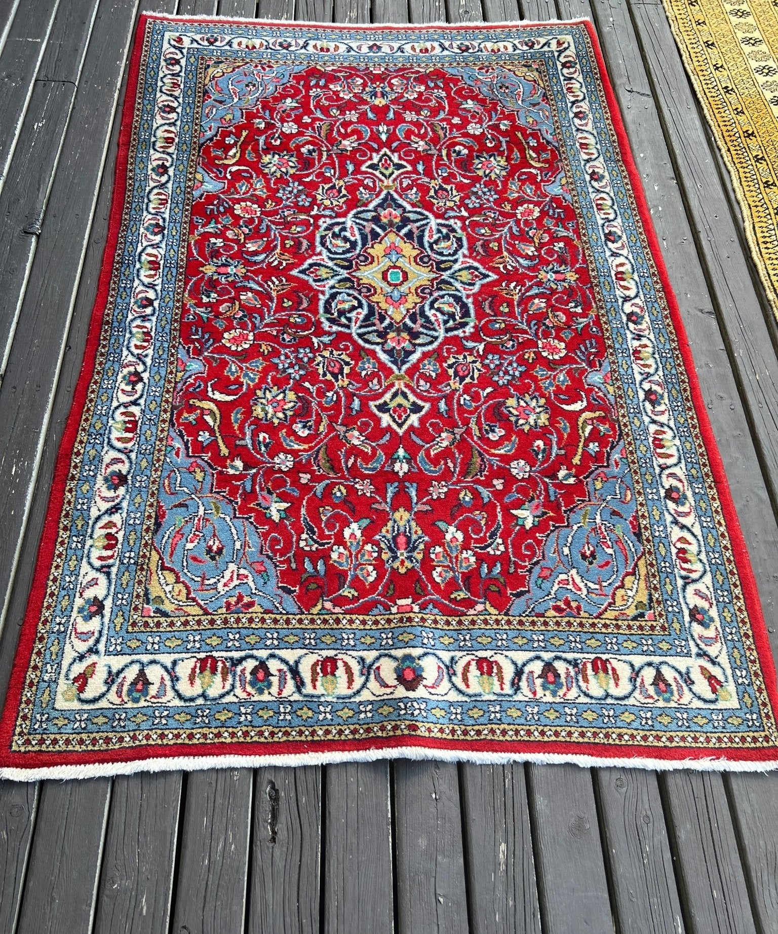 Sarouk rug with red central medallion, cream and blue border, flat on gray deck