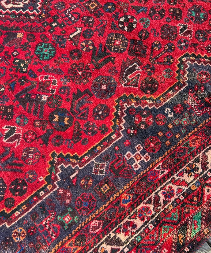 Persian Shiraz rug close-up, deep red background with navy, cream and green motifs
