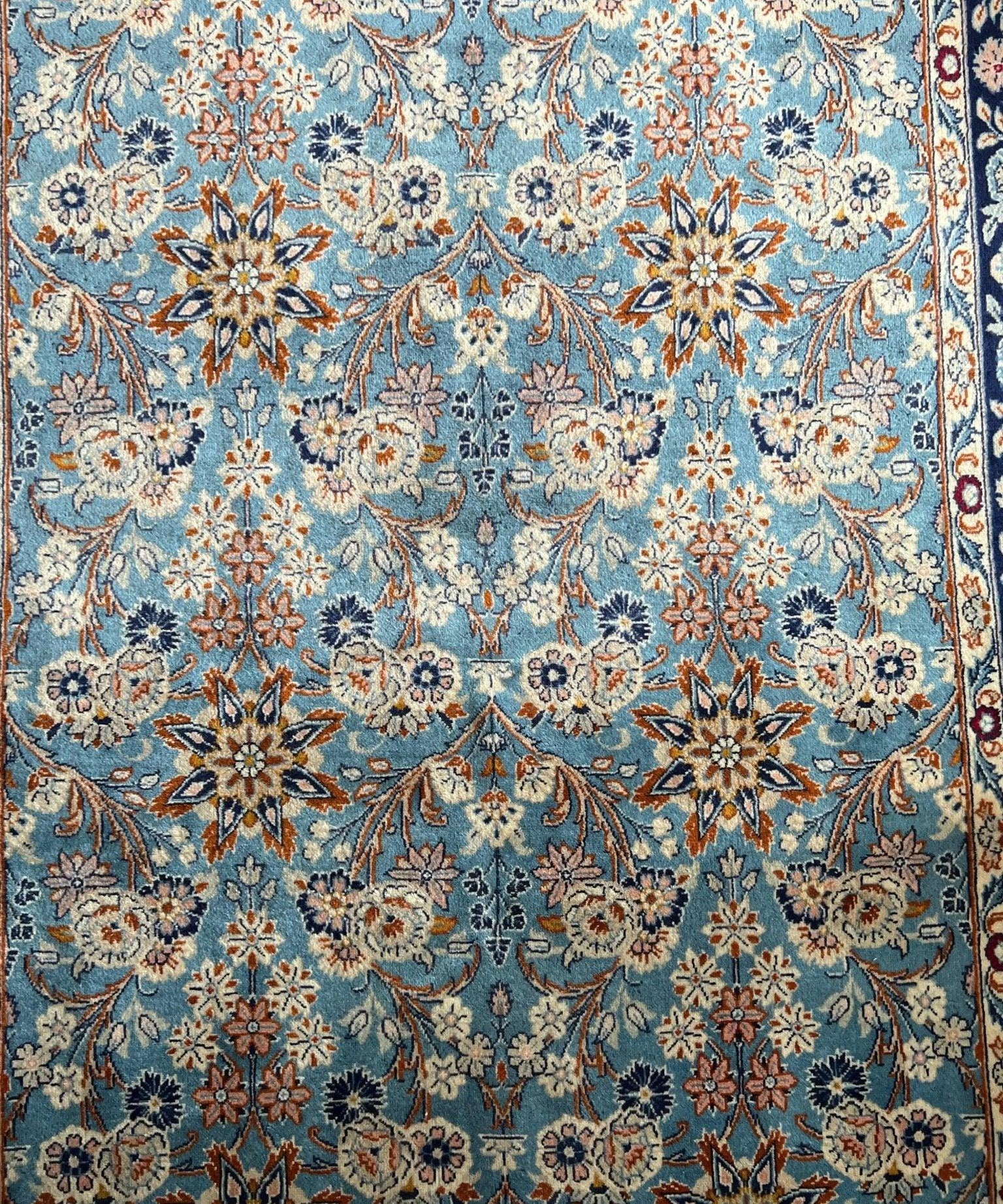 Close-up Persian rug pattern: light blue field with floral rosettes and navy accents