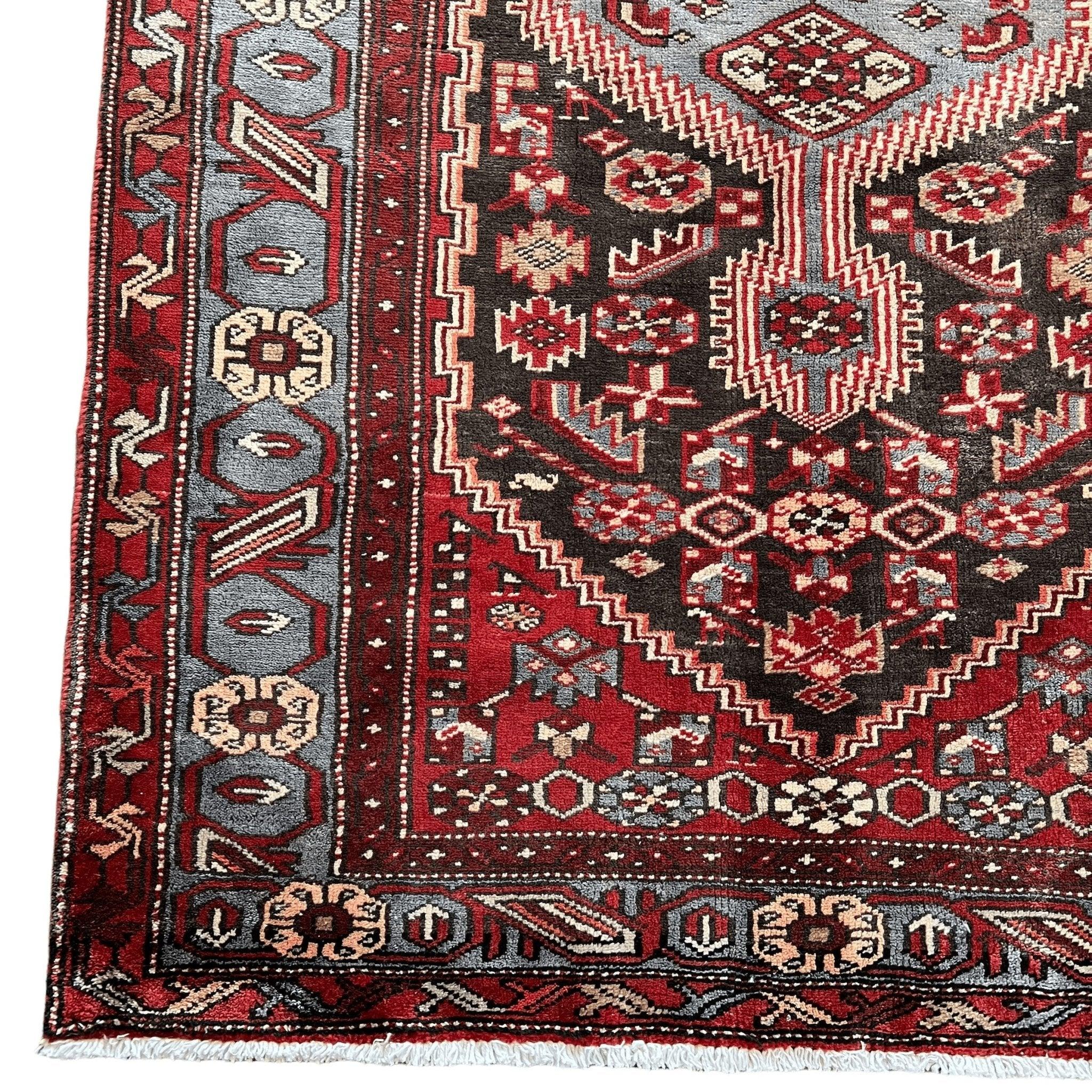 Persian Zanjan rug corner close-up with red, cream, and black geometric border and fringe