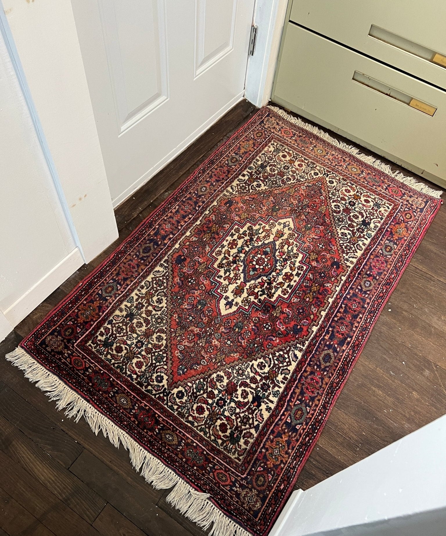 Rectangular red rug with cream ornamental medallions, detailed border, and fringed corners