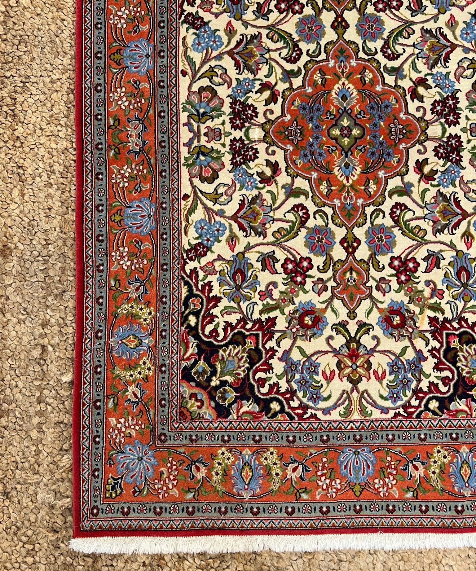 Ornate area rug with cream field, rust red border, floral corner medallion.