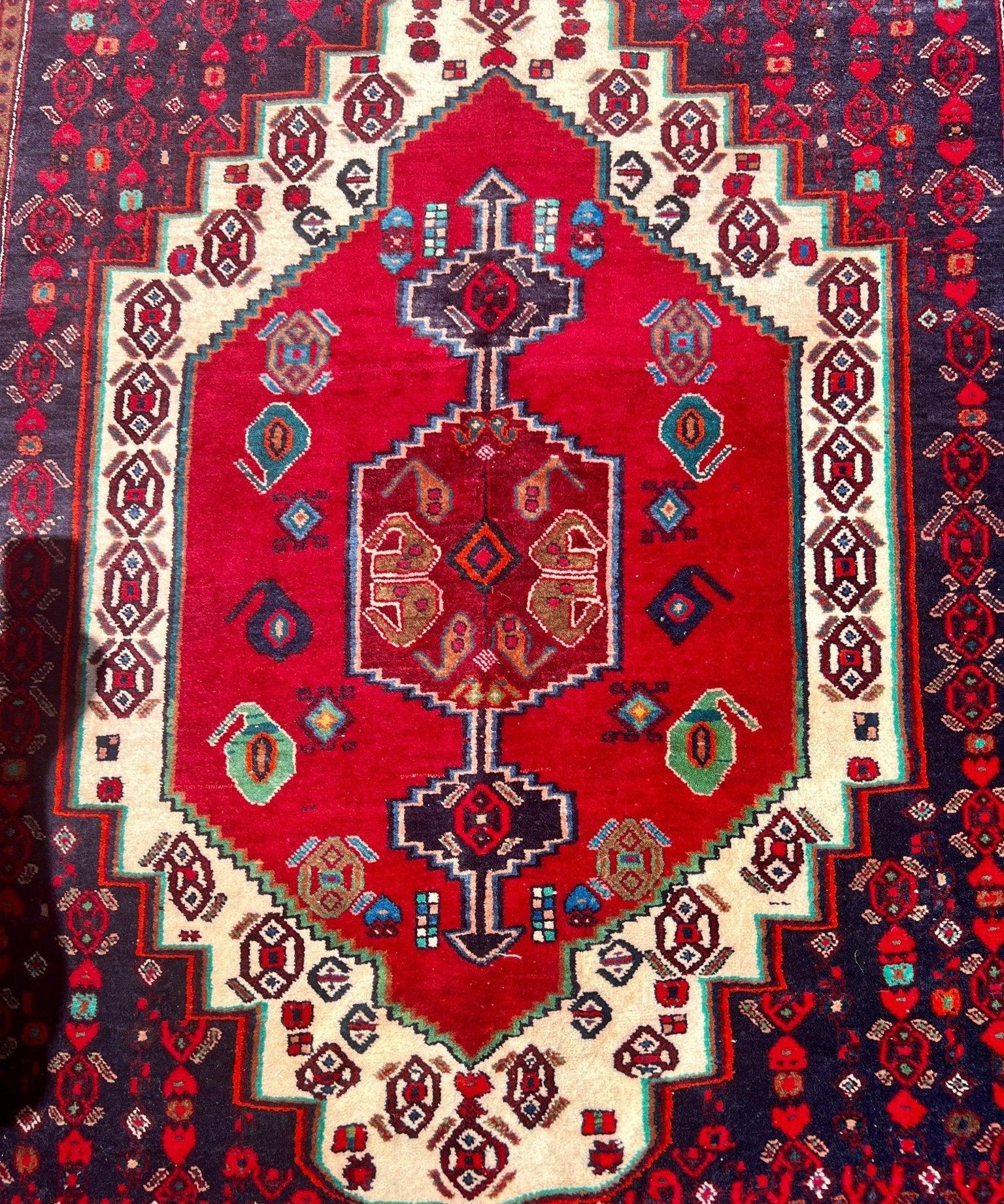 Vintage Senneh rug close-up: red center medallion with cream diamond motifs