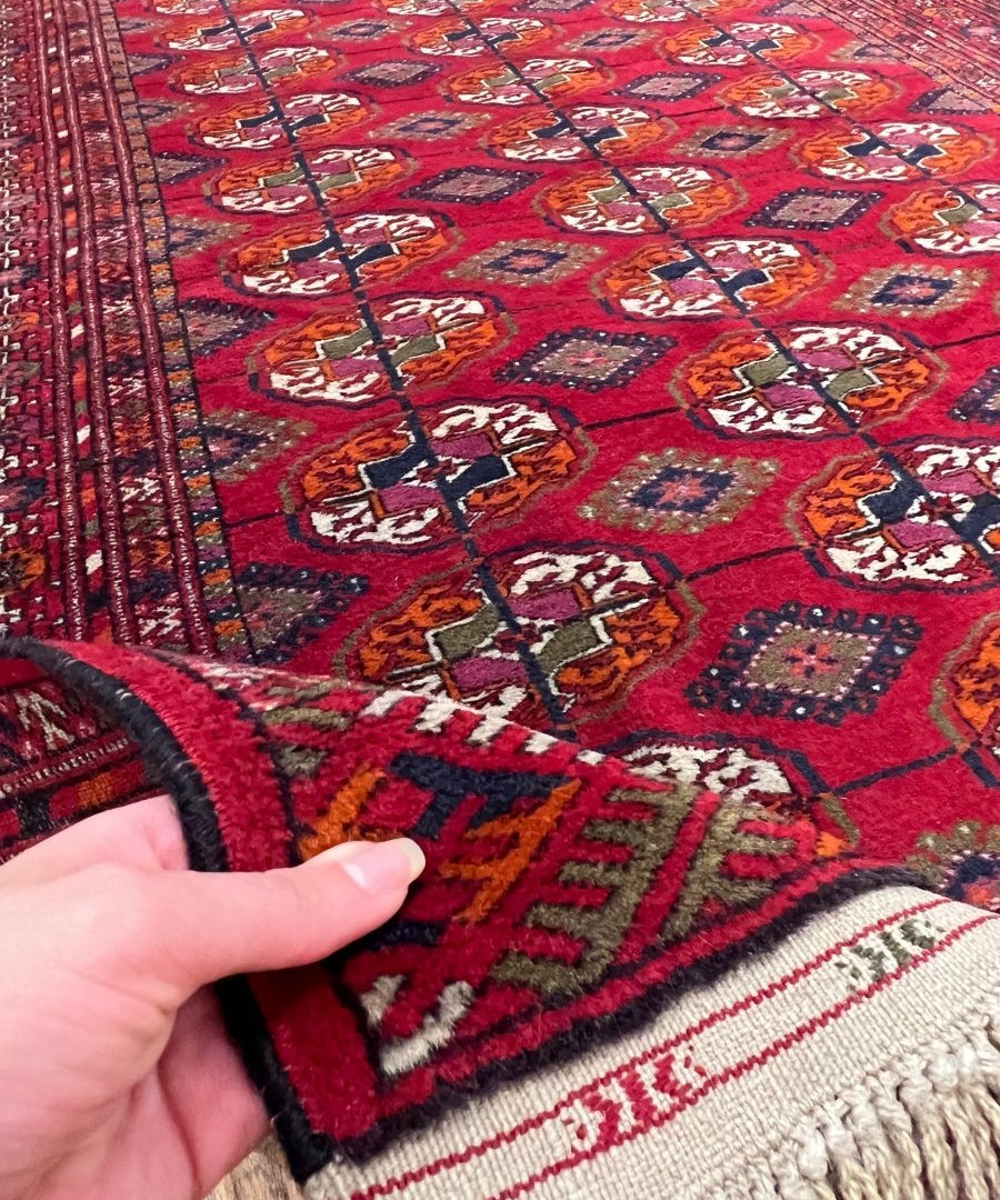 Red Bukhara rug corner with fringed edge and geometric diamond medallion motifs