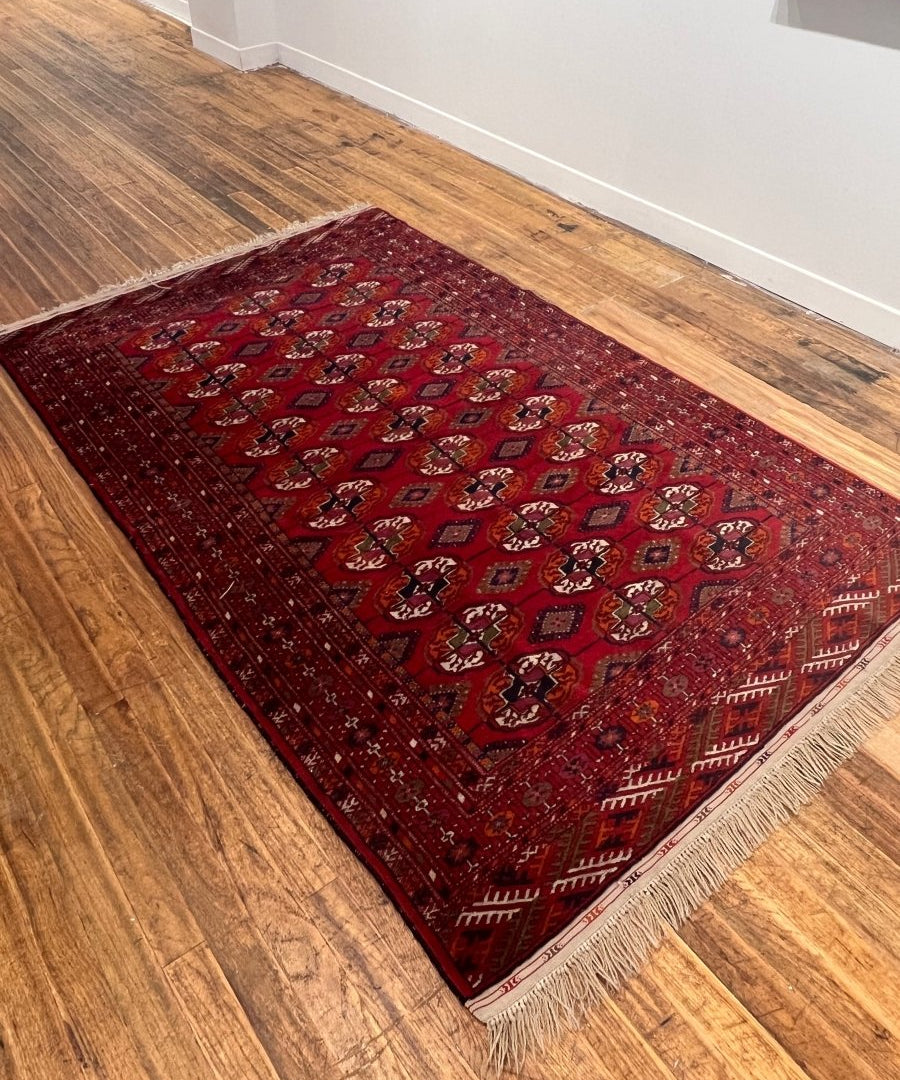 Red Bukhara rug on wood floor with fringed edges and repeating medallion pattern