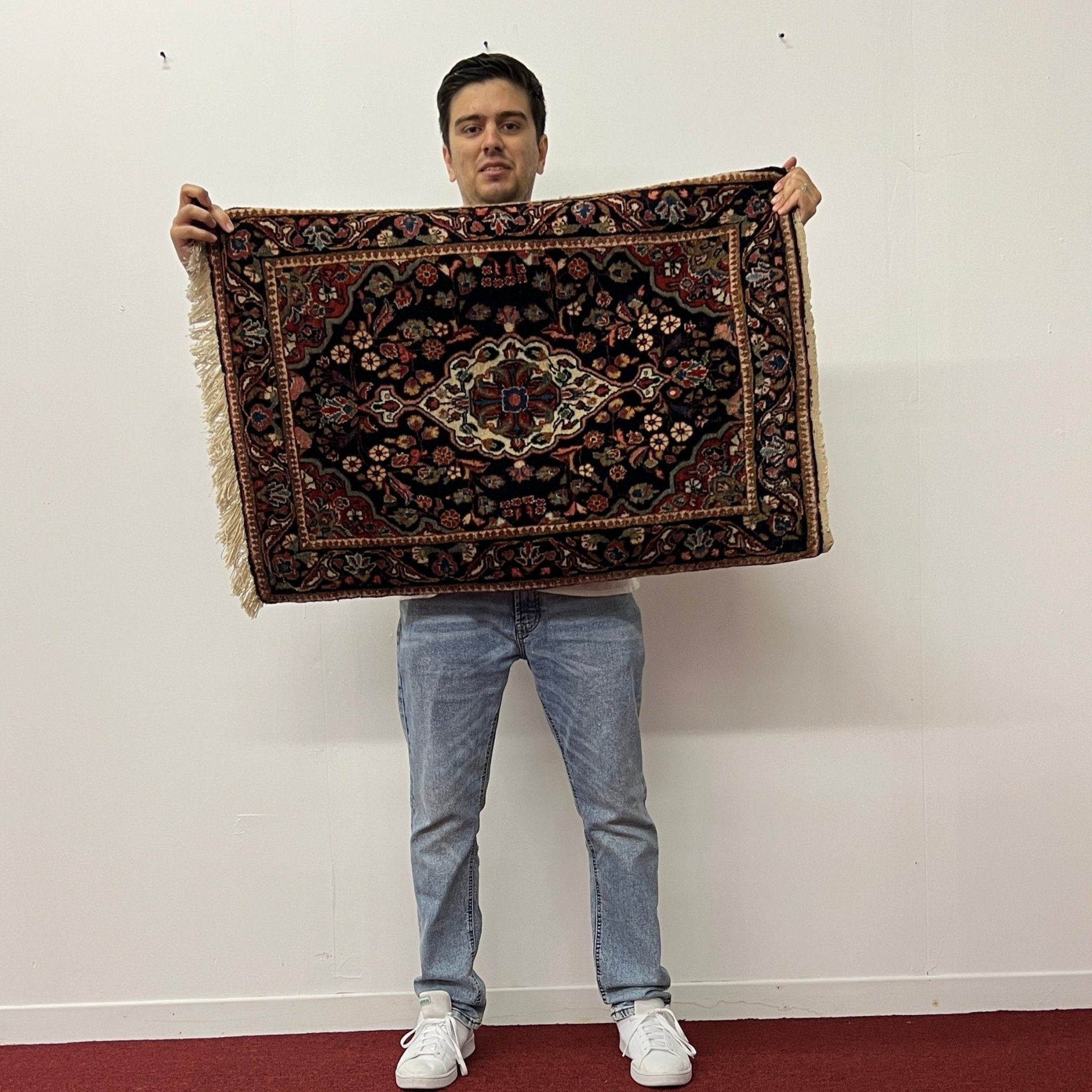Small rug with dark navy field, red and blue floral medallion, fringed edges