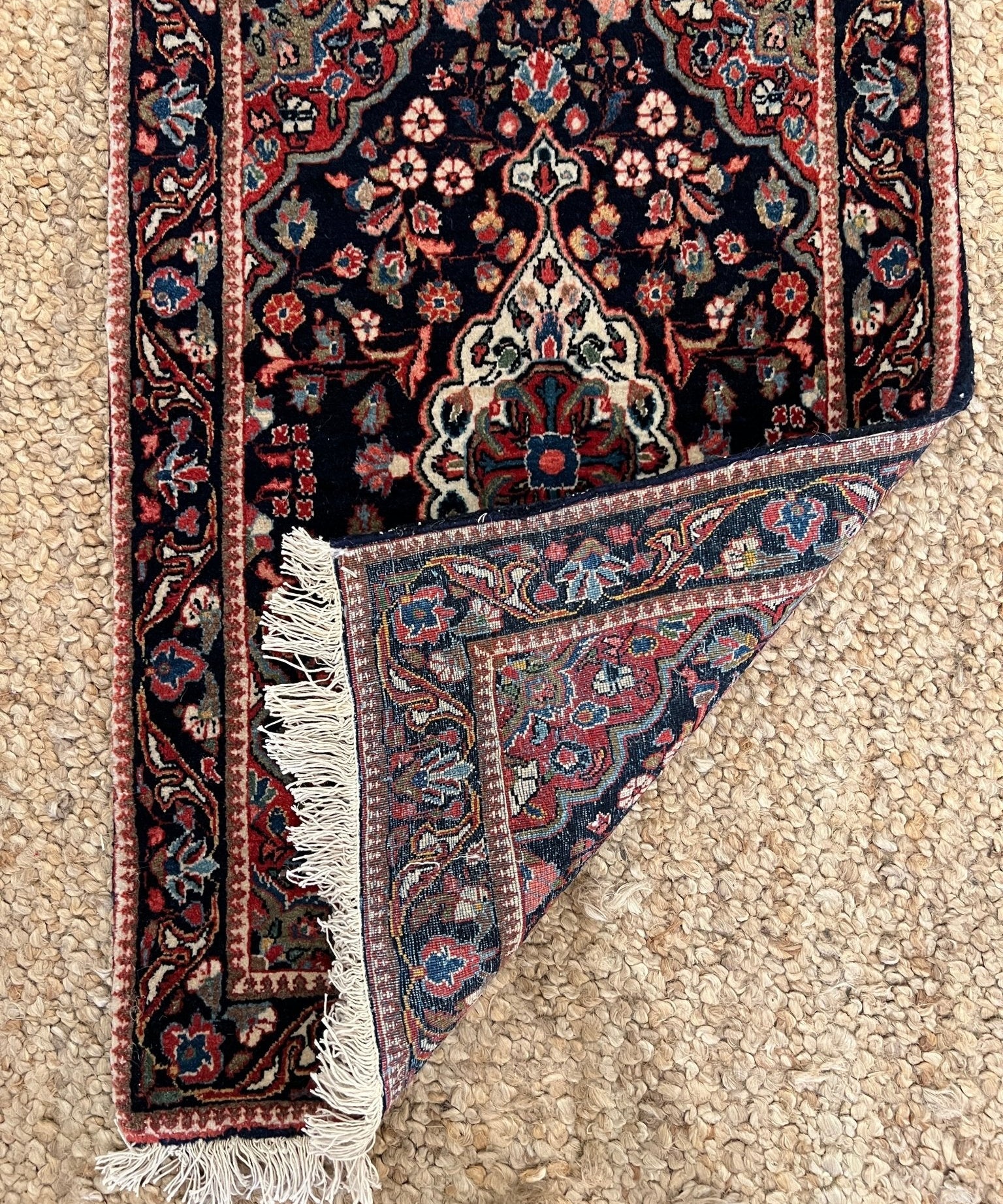 Close-up of dark navy rug corner with ornate floral pattern and white fringe