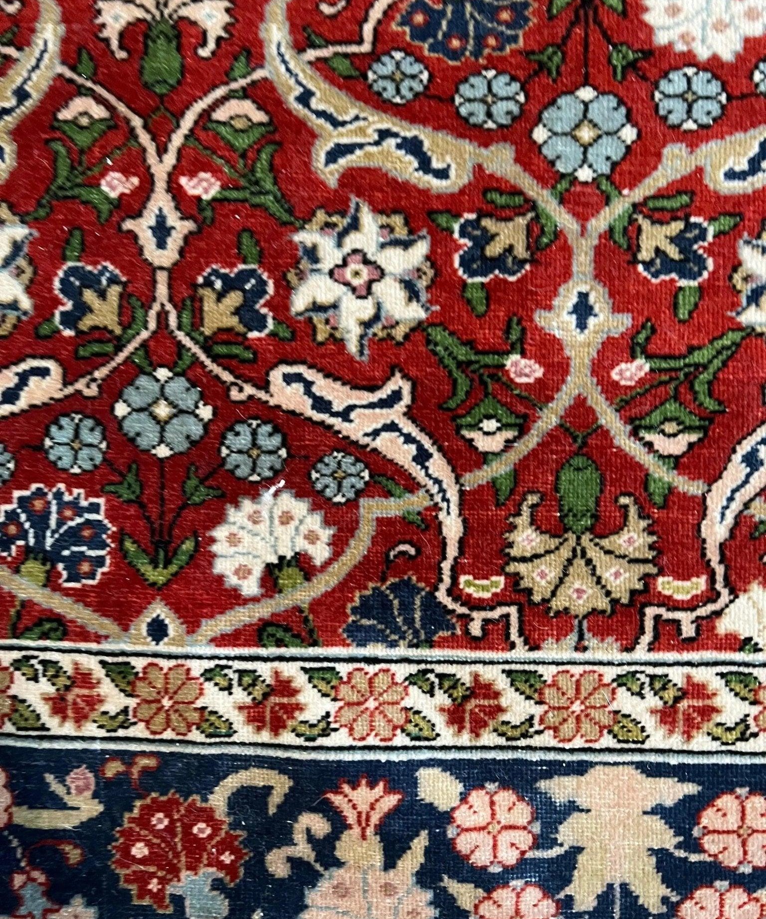 Close-up of red rug with white, green, and blue floral motifs and detailed border