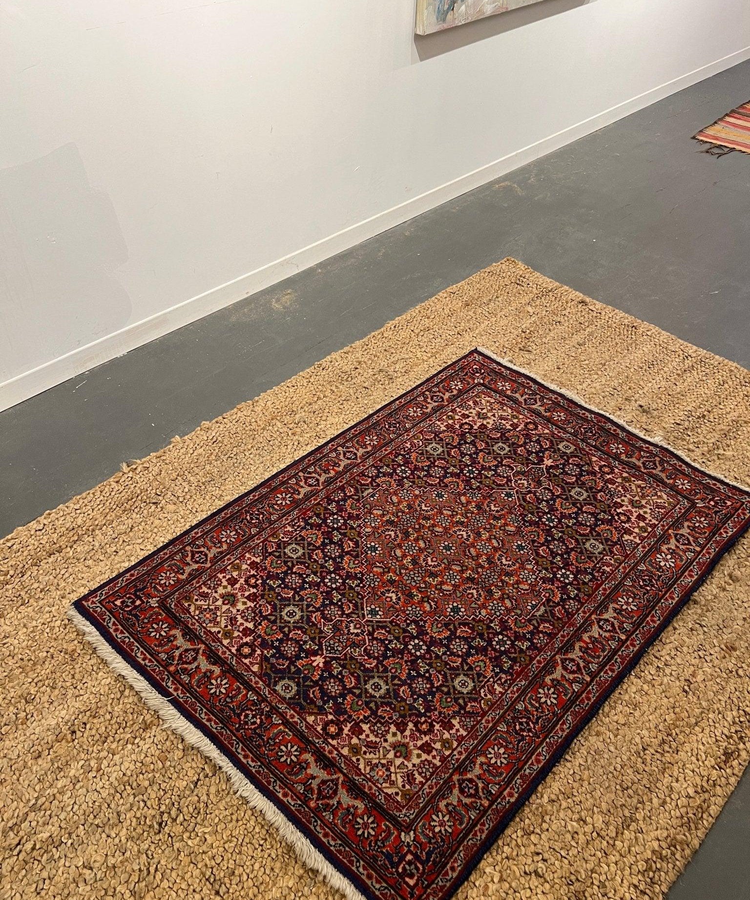 Persian Tabriz rug laid flat on beige carpet, red and blue geometric pattern
