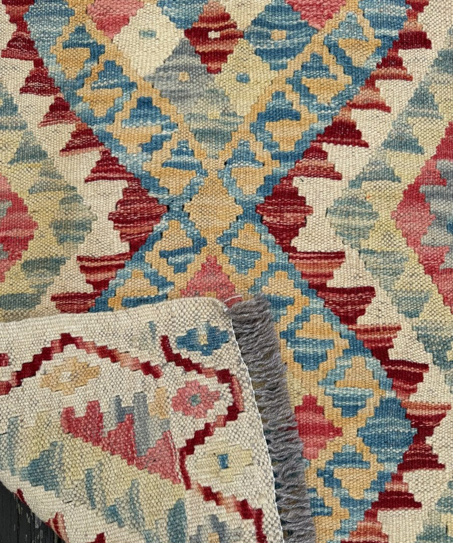 Kilim rug corner detail, cream ground with red, blue, yellow diamonds and fringe