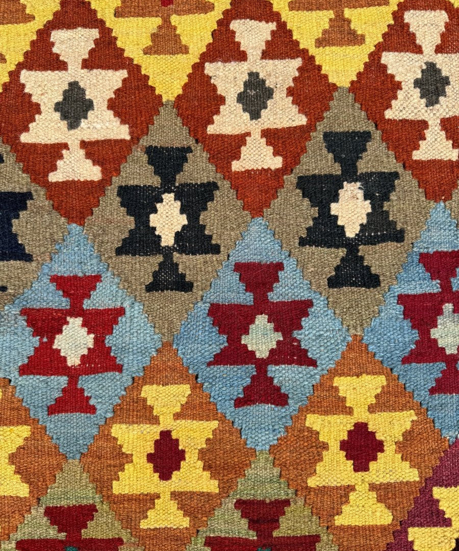 Afghan kilim rug close-up, repeating diamond motifs in navy, red, blue, yellow, cream