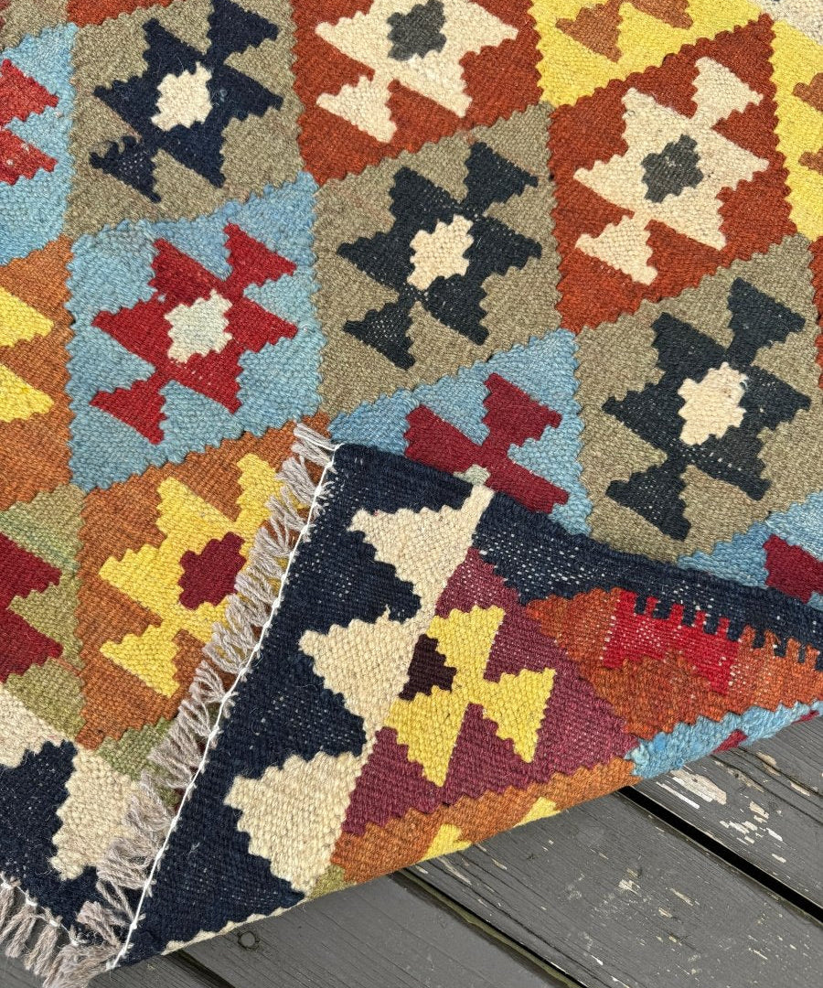 Multicolor Afghan kilim rug corner with geometric pattern and short fringe along edge