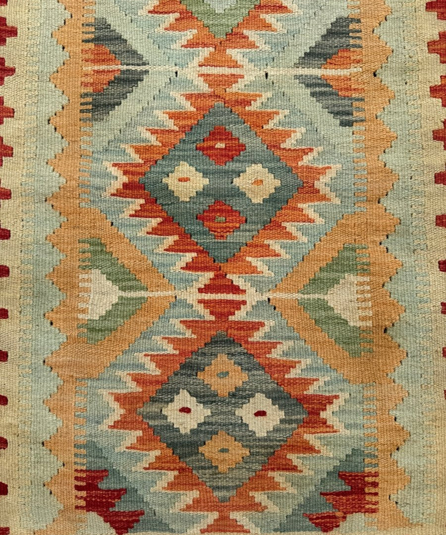 Kilim rug close-up of teal diamond motifs, cream and orange zigzag rows, green details, small fringe