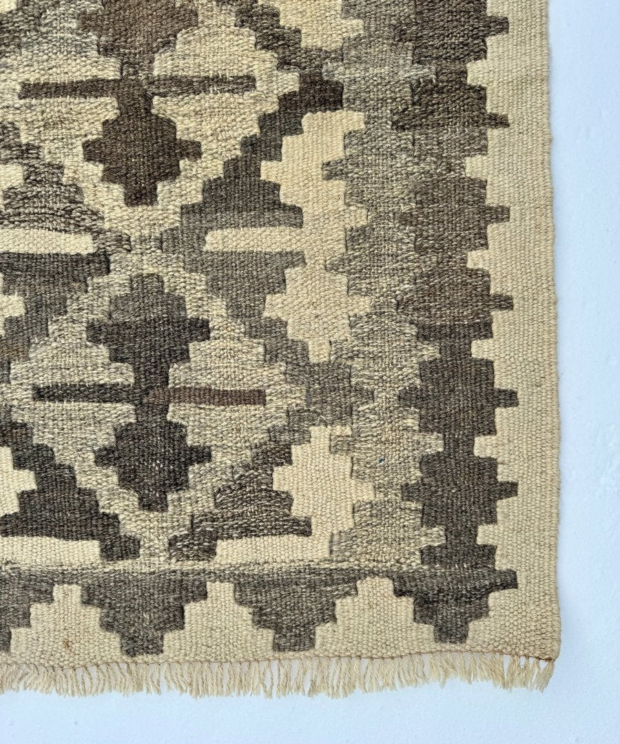 Kilim rug close-up, cream base with dark gray blocks and borders, fringed edge