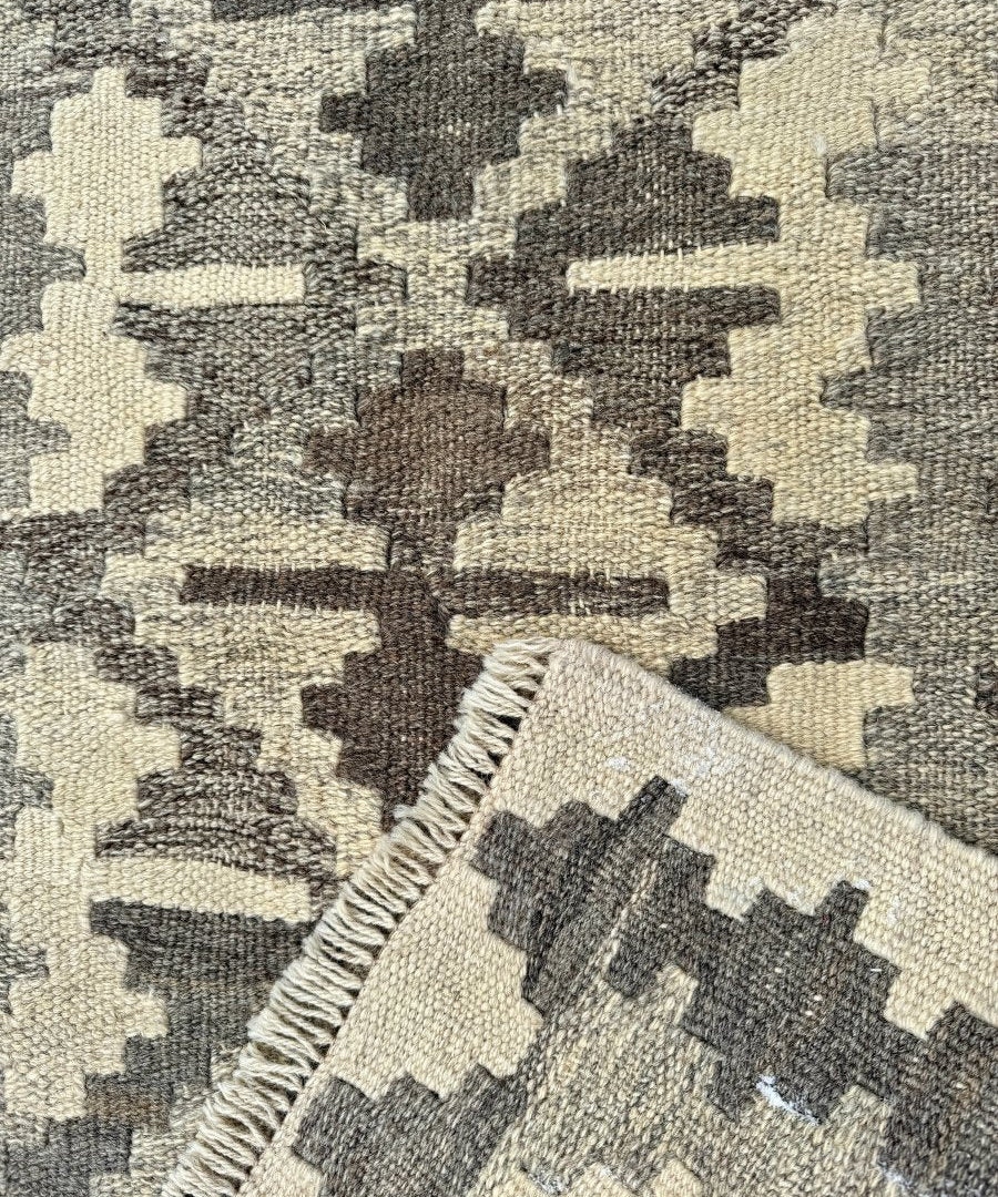 Kilim rug corner close-up, cream and dark gray geometric motif with braided fringe