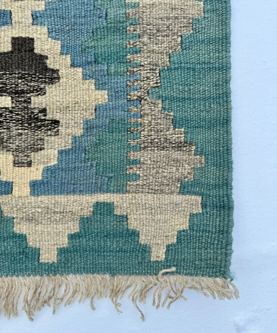 Kilim rug corner close-up with teal field and cream, blue, black geometric motifs, fringe