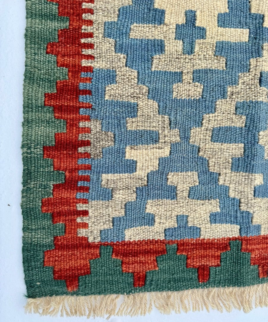 Kilim rug detail with blue and cream geometric motifs on green ground, red side border